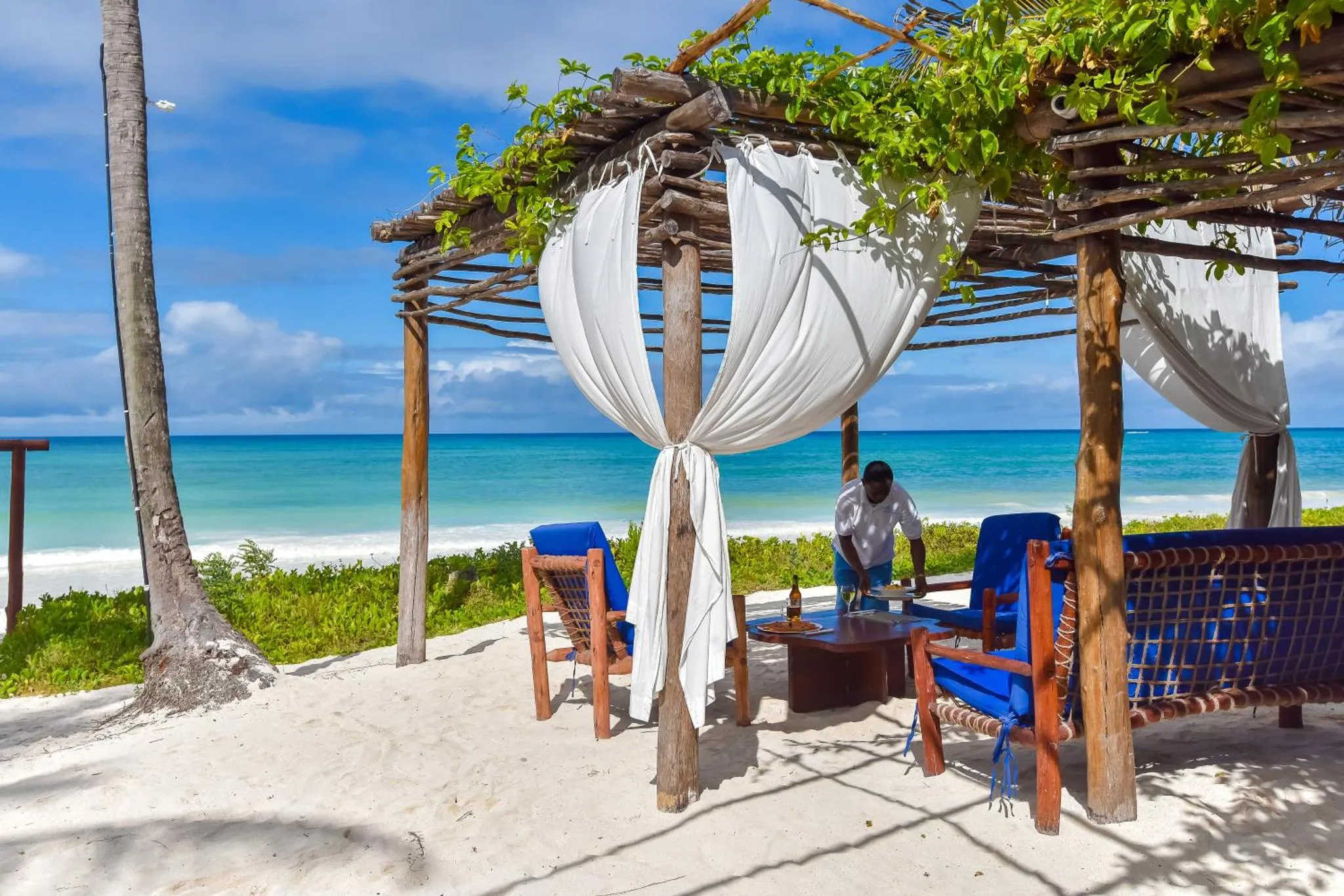 Un espace de détente ombragé surplombe une plage de sable blanc et une mer turquoise.