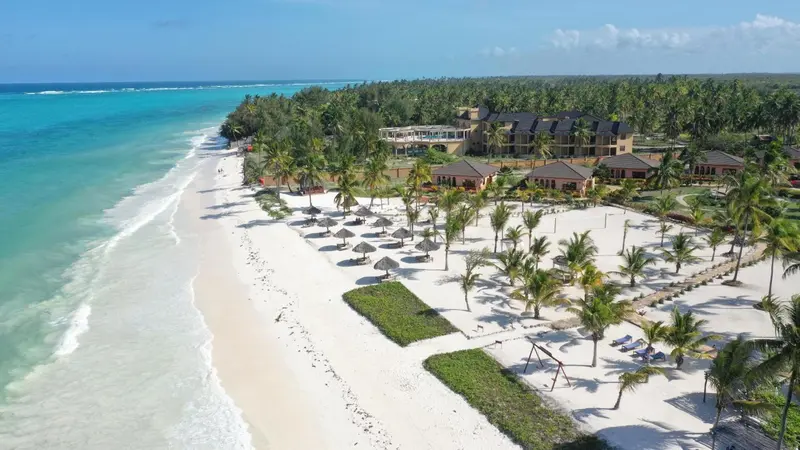 Vue aérienne d'une plage de sable blanc bordée de palmiers et d'un complexe hôtelier.