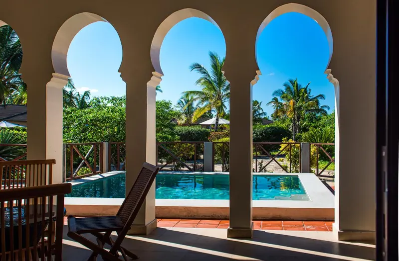 Vue sur une piscine et une végétation luxuriante à travers des arcades.