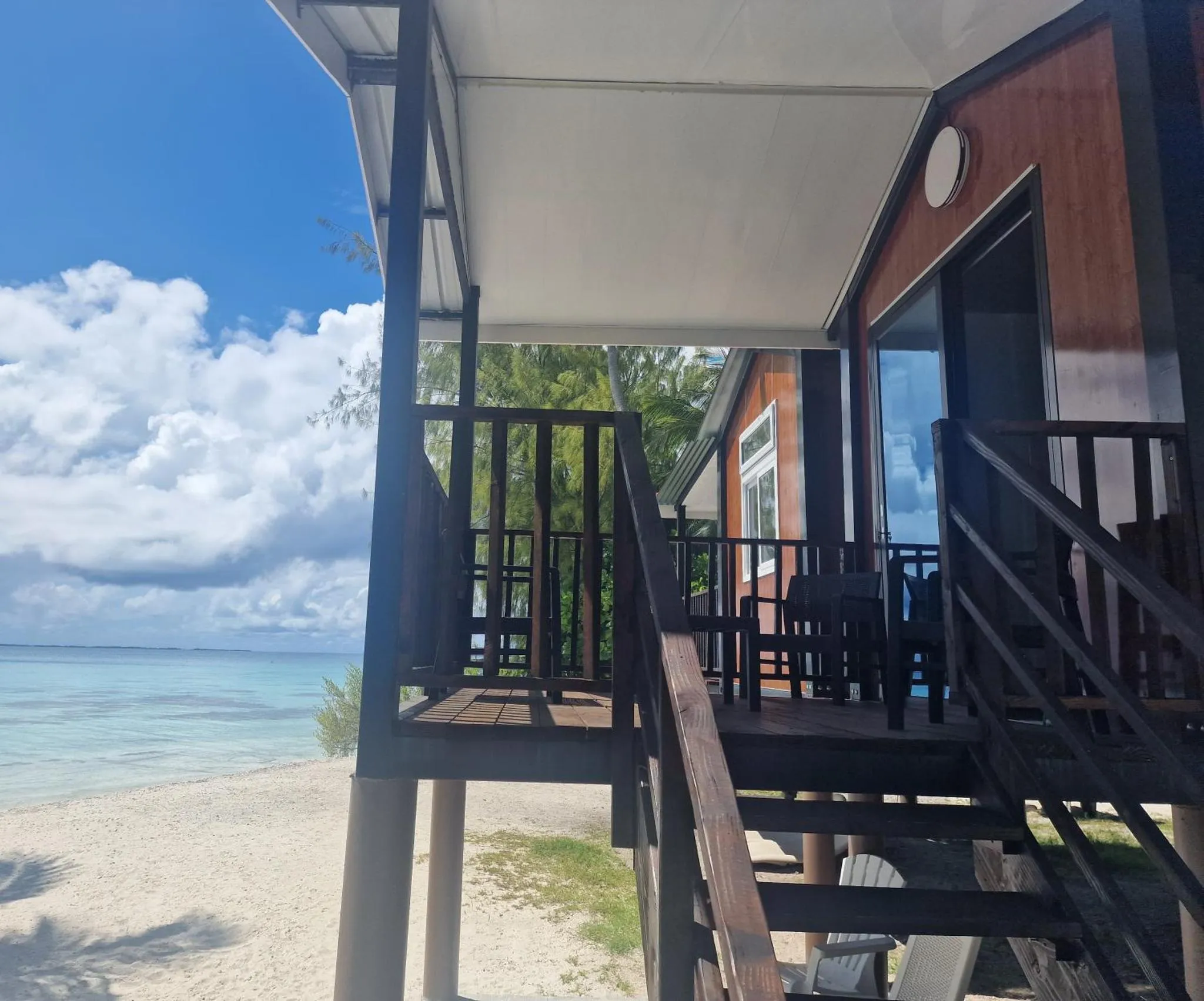 Terrasse ombragée donnant sur une plage de sable blanc et une mer turquoise.