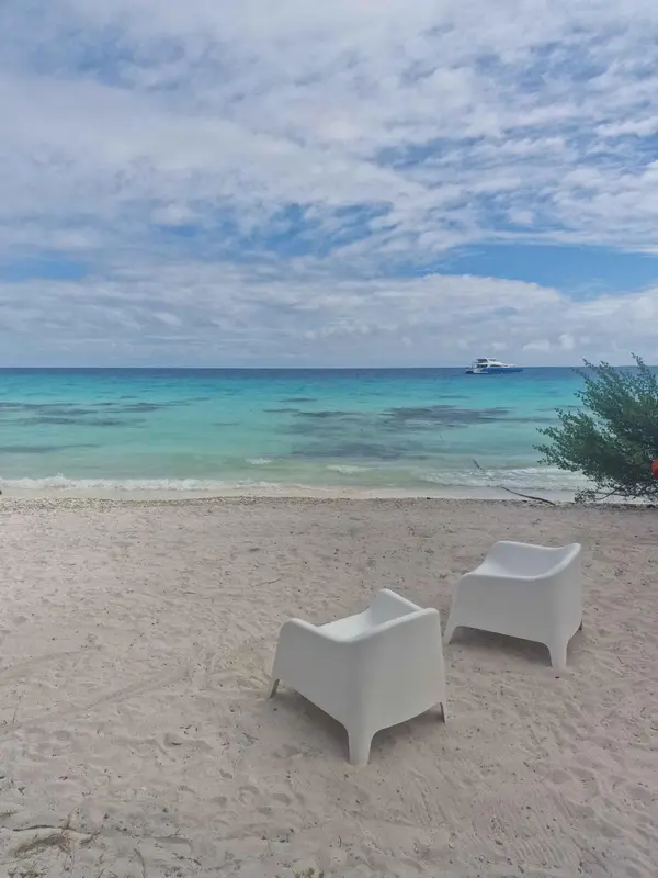 Deux fauteuils blancs sur une plage de sable fin face à une mer turquoise.