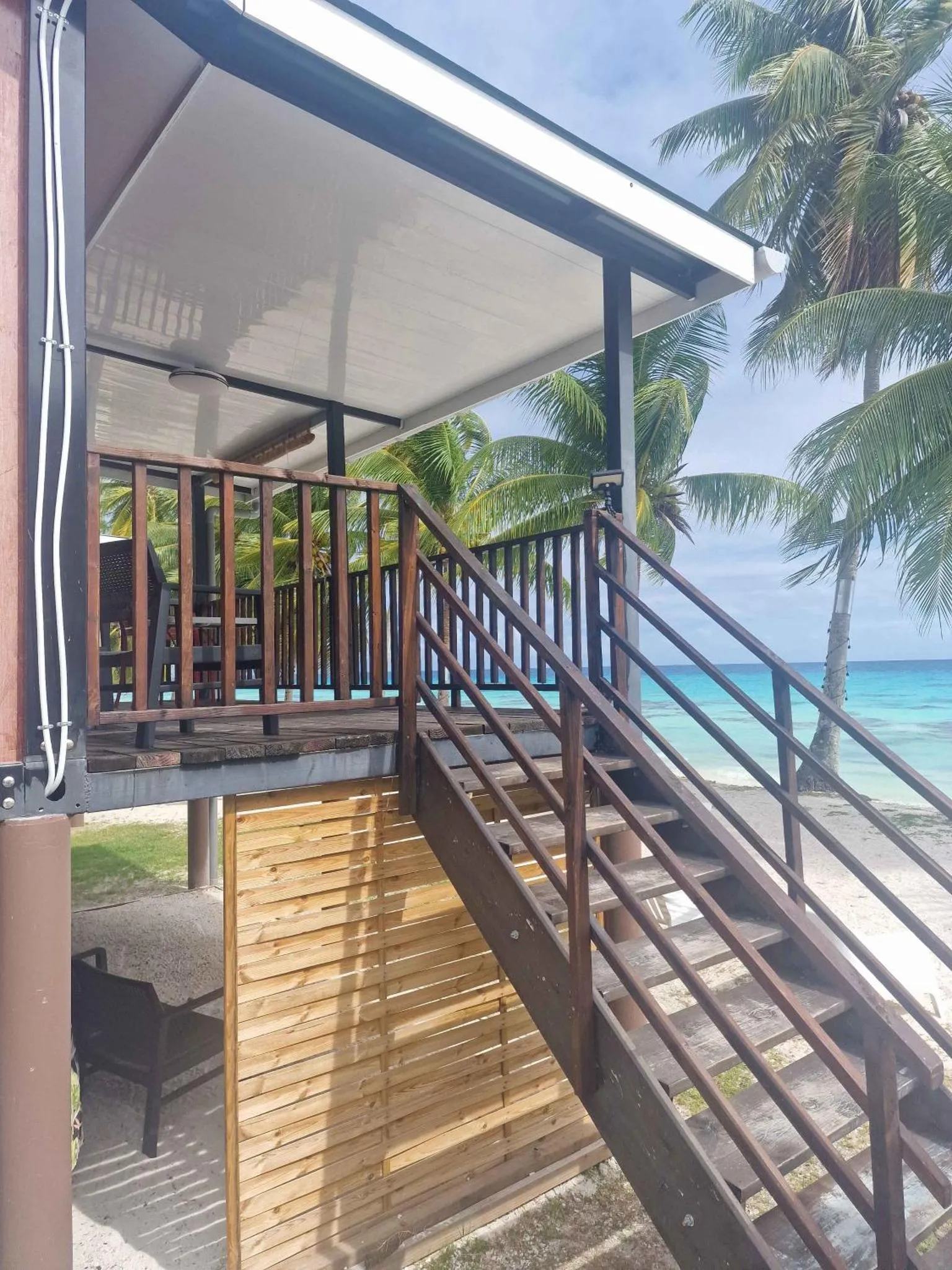 Un escalier en bois mène à une terrasse ombragée face à la mer.