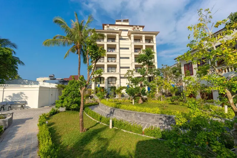 Bâtiment blanc à plusieurs étages entouré de végétation tropicale et d'une pelouse verdoyante.