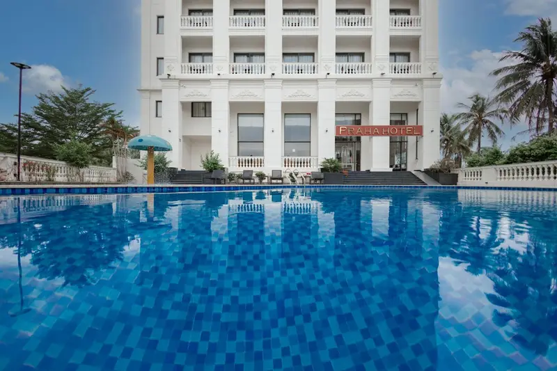 Vue d'une piscine turquoise reflétant un bâtiment blanc et des palmiers sous un ciel bleu.