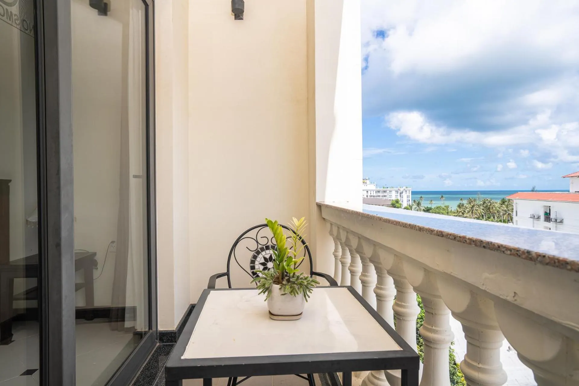 Une terrasse avec une petite table et une plante en pot offre une vue sur la mer et le ciel nuageux.