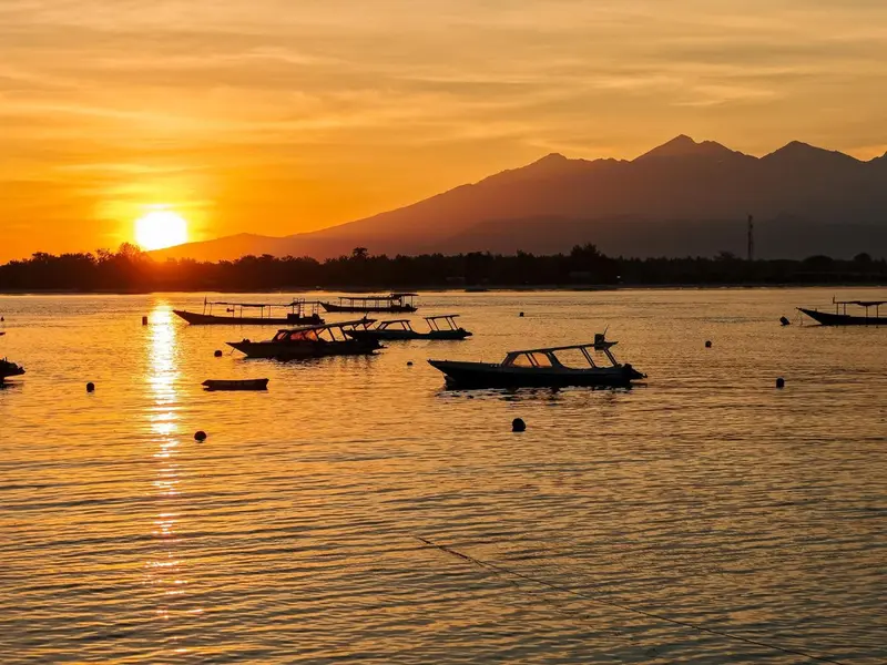 Le soleil se couche sur une mer calme avec des bateaux traditionnels à l'horizon.