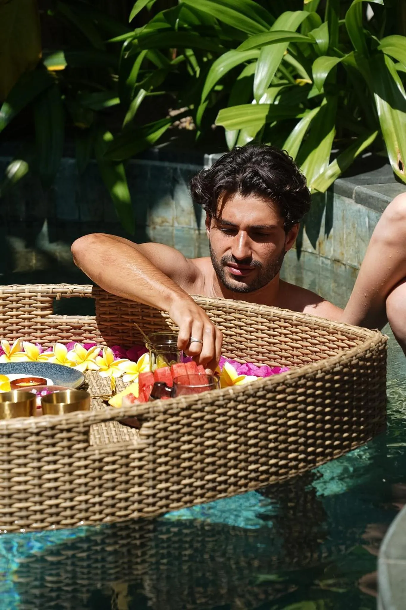Un homme se détend dans une piscine avec un plateau de fruits et de boissons.