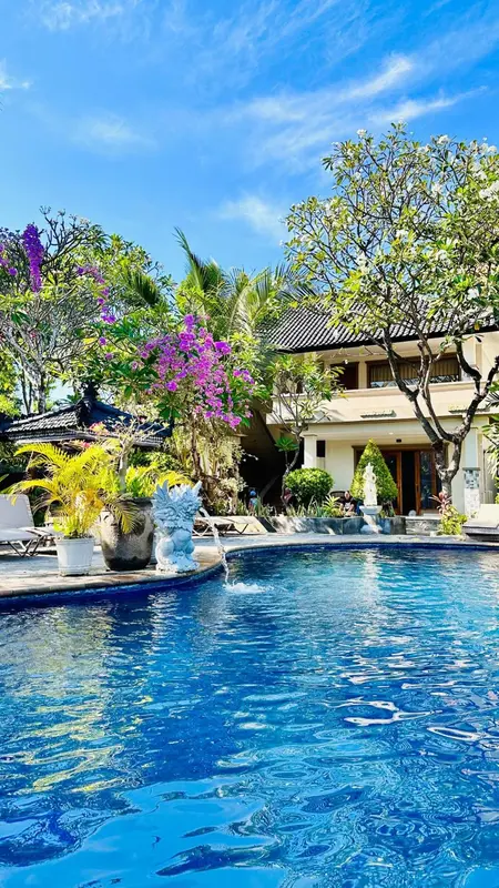 Une piscine turquoise bordée de végétation luxuriante devant un bâtiment blanc.
