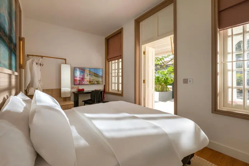 Une chambre lumineuse avec un lit fait et une vue sur une végétation luxuriante.