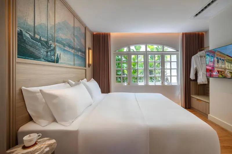 Une chambre lumineuse avec un grand lit et une fenêtre donnant sur la végétation.