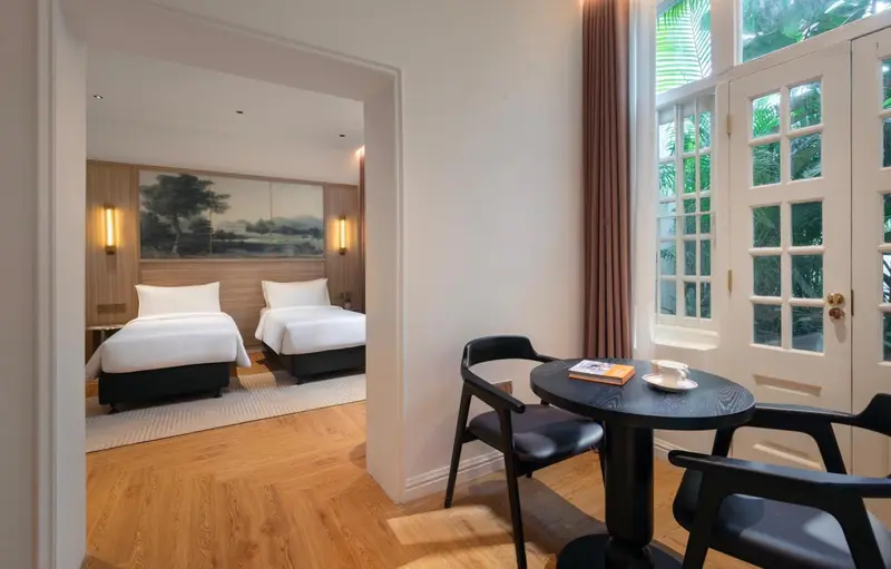 Une chambre lumineuse avec deux lits et un coin repas près d'une fenêtre.