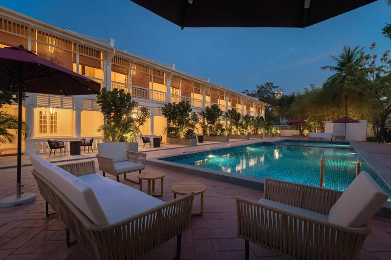 Mobilier de jardin disposé devant une piscine illuminée et un bâtiment à l'architecture coloniale.