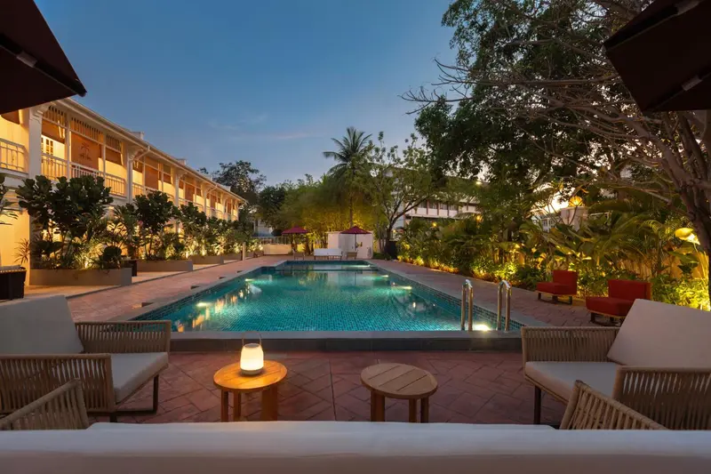 Une piscine rectangulaire bordée d'un espace de détente avec des fauteuils et des tables basses.