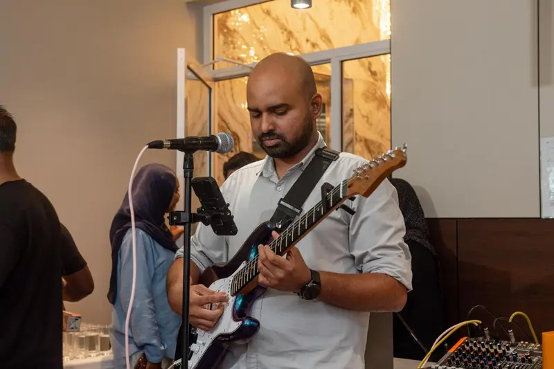 Un homme joue de la guitare électrique devant un micro sur une scène.