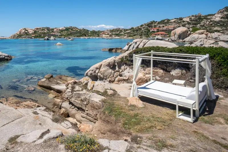 Un lit d'extérieur blanc est installé sur une plage rocheuse face à la mer.