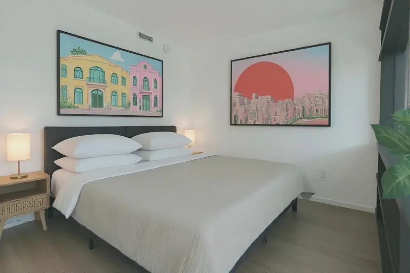 Une chambre lumineuse avec un grand lit et deux tableaux colorés au mur.