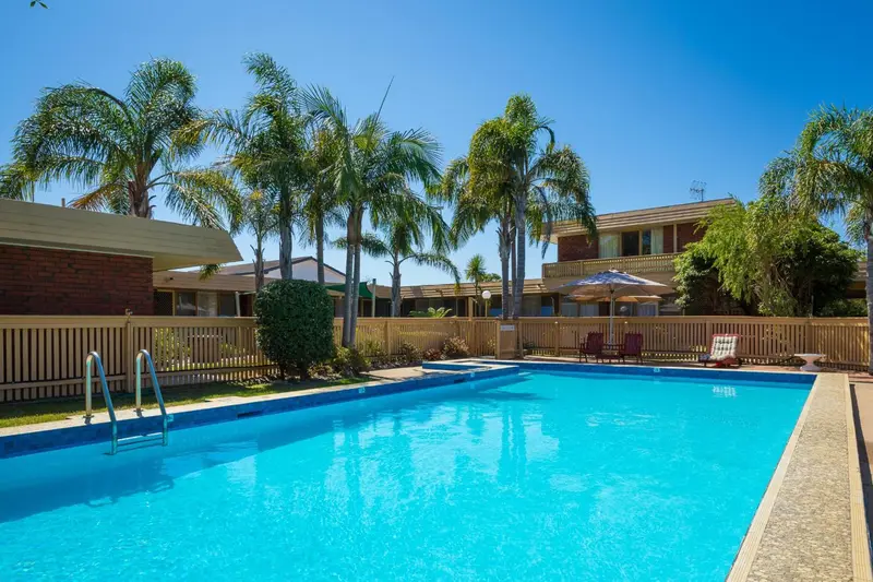 Une piscine rectangulaire turquoise est entourée d'une terrasse et de végétation luxuriante.