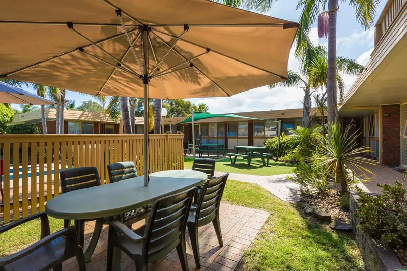 Tables et parasols sur une terrasse verdoyante près d'une piscine.