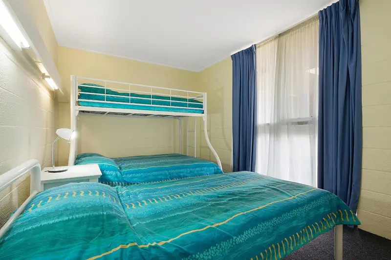 Une chambre avec un lit superposé et un lit double est éclairée par des lampes murales.