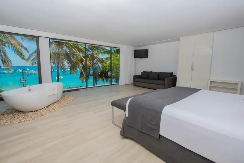 Une chambre lumineuse avec un grand lit et une baignoire face à la mer.
