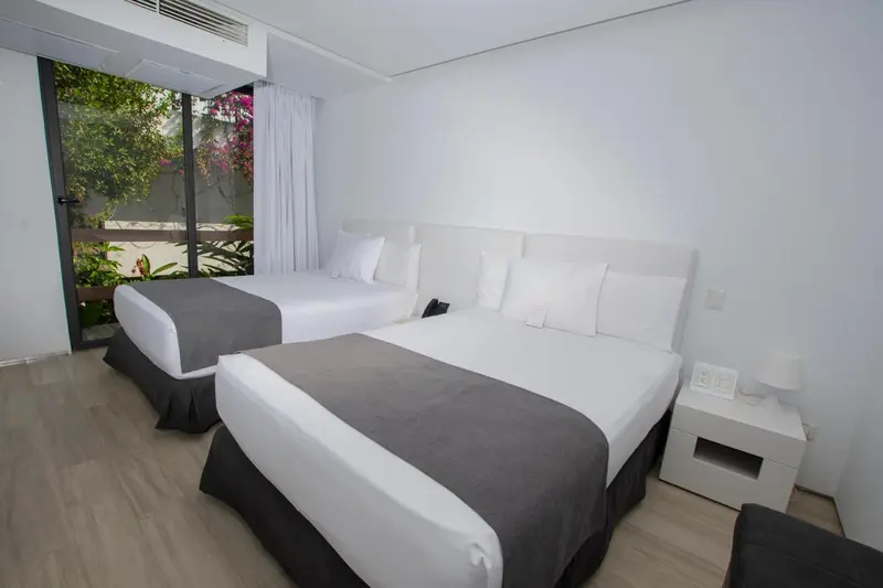 Chambre lumineuse avec deux lits simples et une vue sur la végétation.