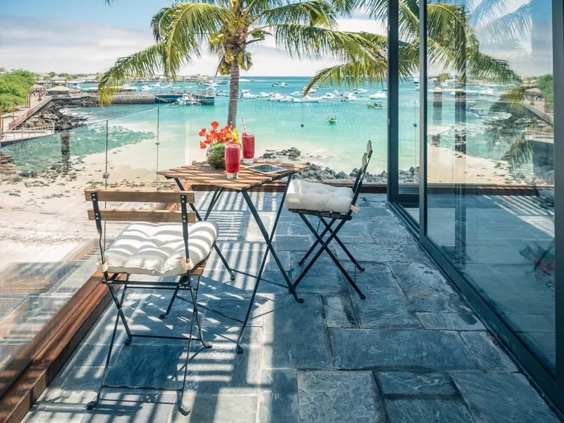 Une table et des chaises en bois sont disposées sur une terrasse carrelée face à la mer.