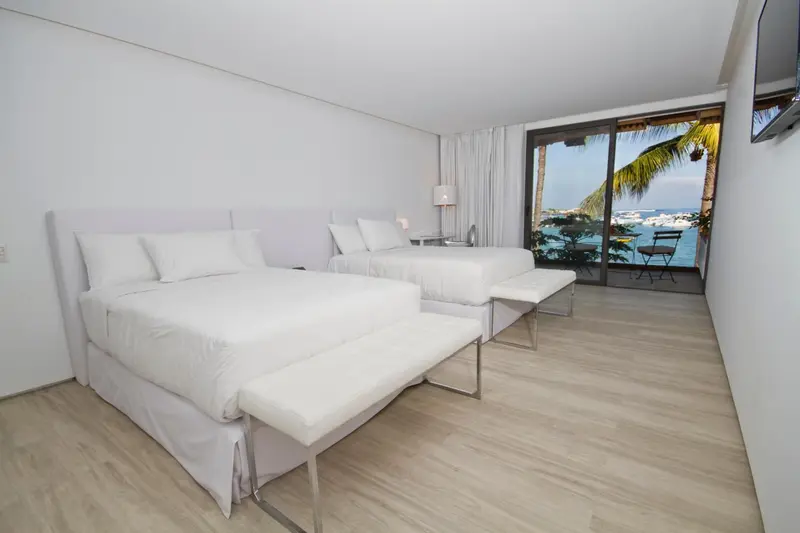 Chambre lumineuse avec deux lits et vue sur la mer.