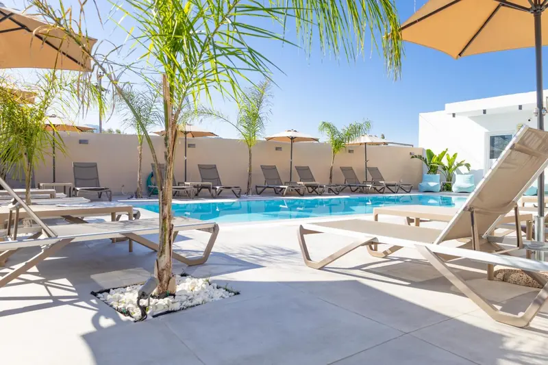 Transats blancs disposés autour d'une piscine ensoleillée, avec des parasols et une végétation tropicale.