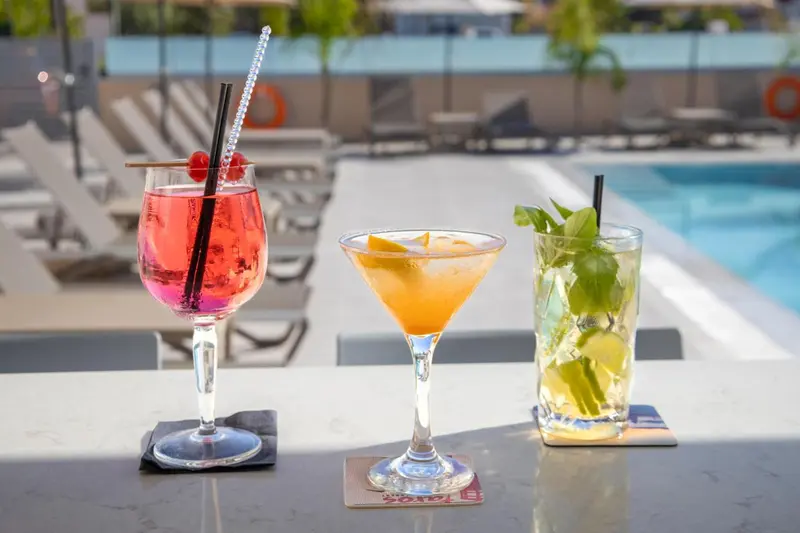 Trois cocktails colorés sont présentés sur un comptoir au bord d'une piscine.