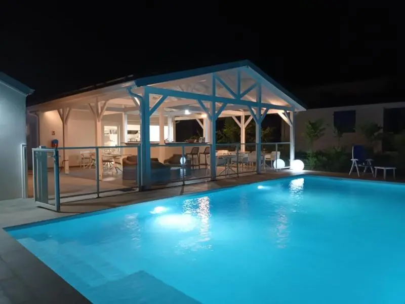 Une piscine illuminee avec un espace couvert et une terrasse.