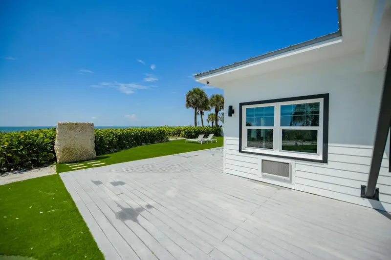 Terrasse en bois blanc devant un bâtiment clair avec une végétation luxuriante et une vue sur la mer.