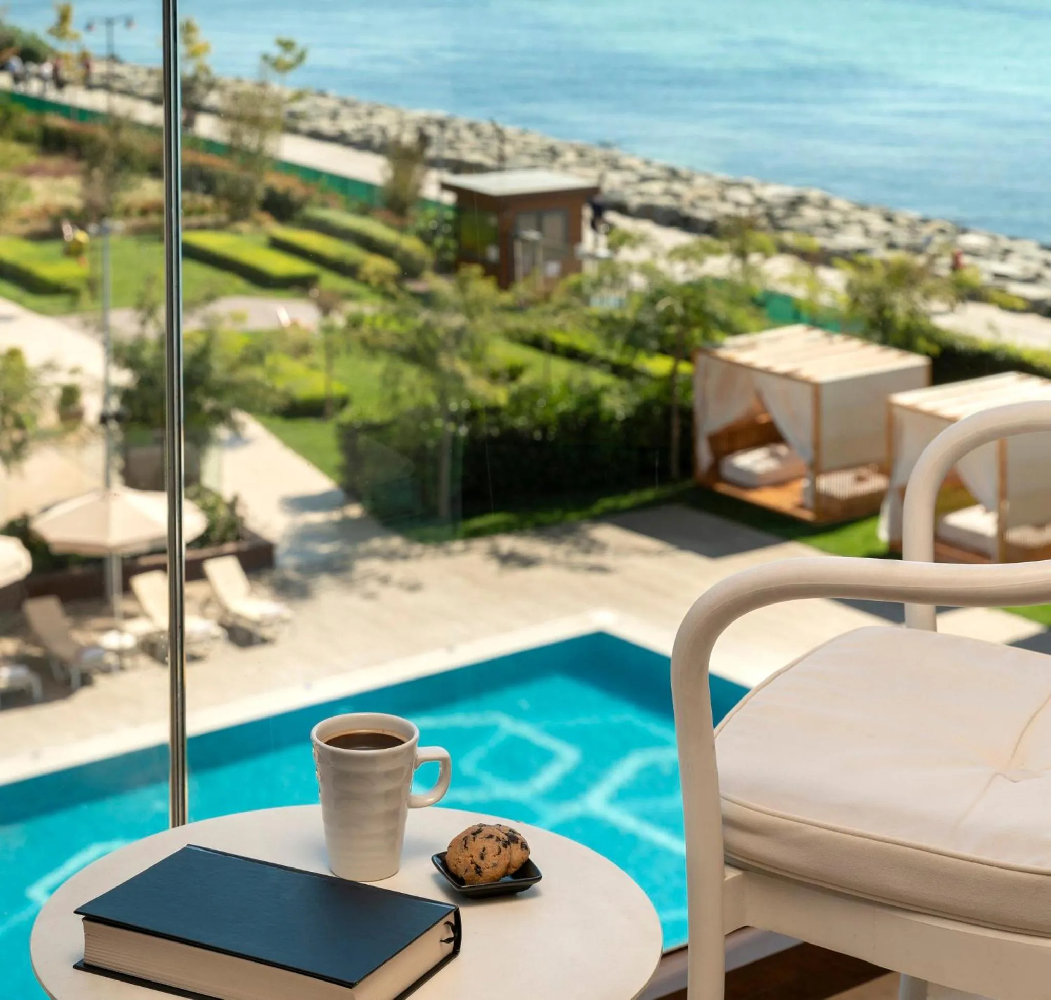 Une table basse avec une tasse de café et un livre sur une terrasse avec vue sur la mer.
