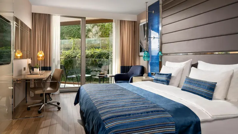 Chambre lumineuse avec un grand lit et un accès à un balcon verdoyant.