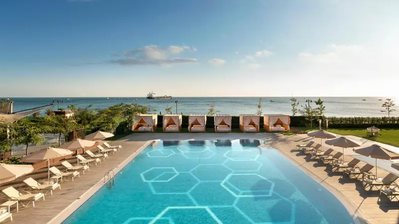 Transats et parasols bordent une piscine rectangulaire avec un fond hexagonal.