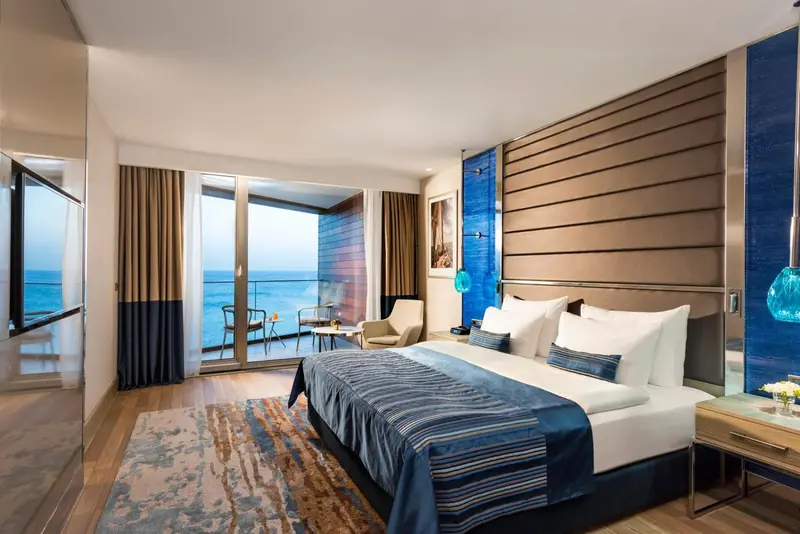 Une chambre lumineuse avec un grand lit et un accès à un balcon avec vue sur la mer.