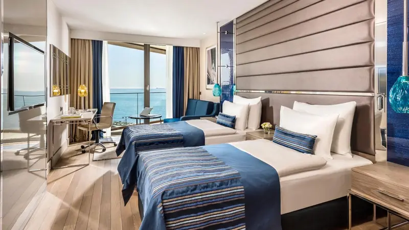 Chambre lumineuse avec deux lits simples et vue sur la mer.
