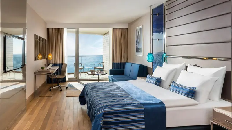 Une chambre lumineuse avec un grand lit et un accès à un balcon avec vue sur la mer.