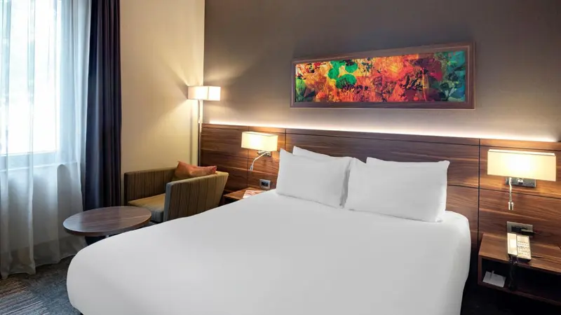 Une chambre lumineuse avec un grand lit recouvert de draps blancs et un fauteuil.