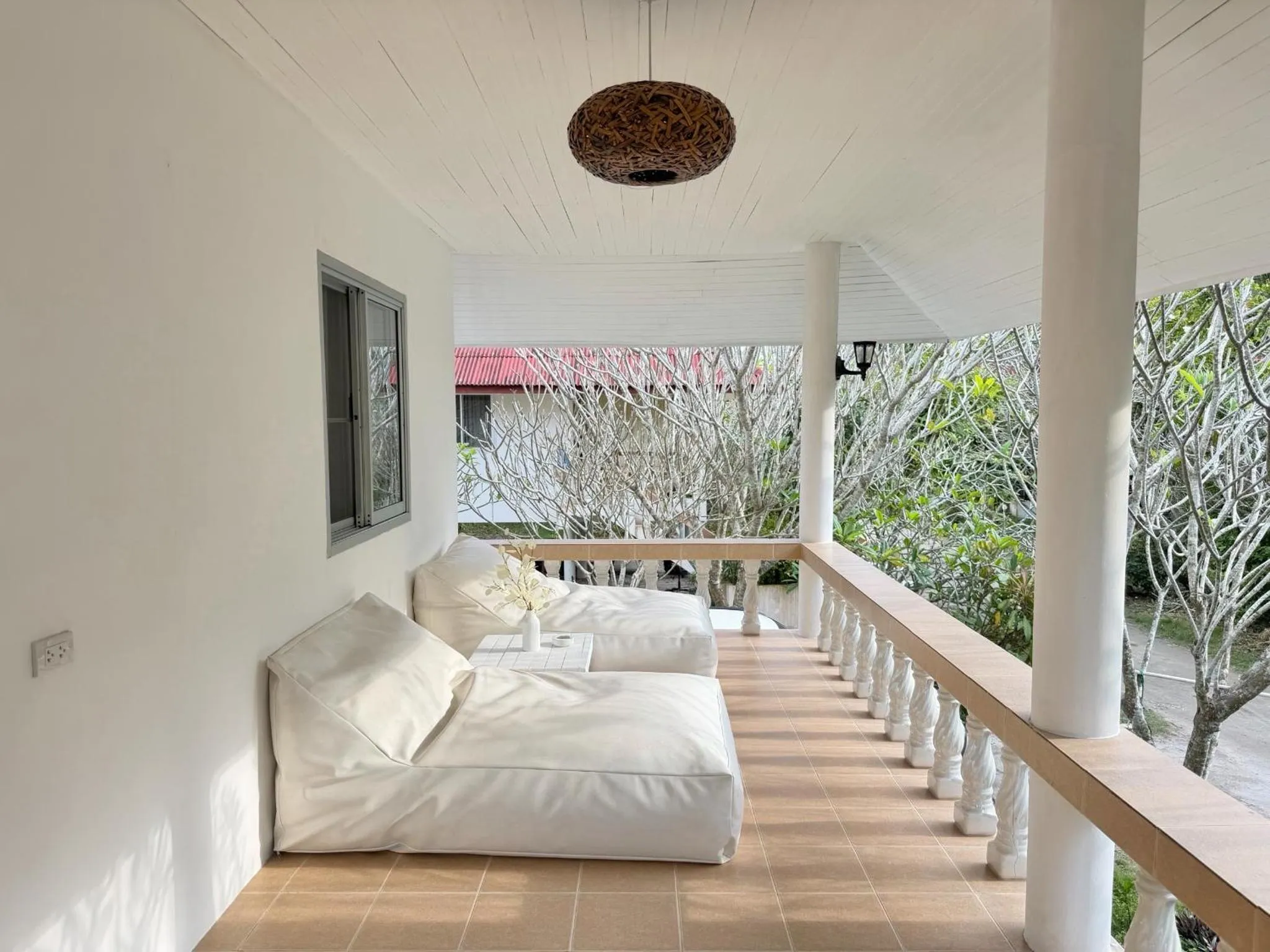 Espace de détente extérieur avec des coussins blancs et une vue sur la végétation.