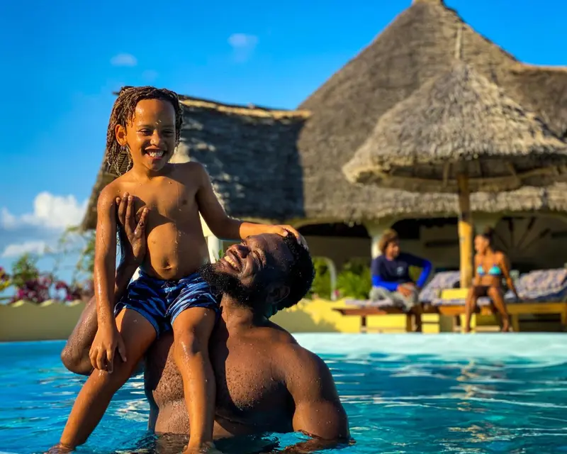 Un homme et un enfant sourient dans une piscine en bord de mer.