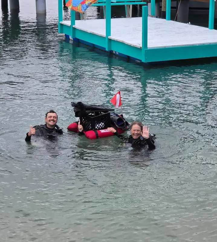 Deux personnes souriantes émergent de l'eau près d'une plateforme verte.