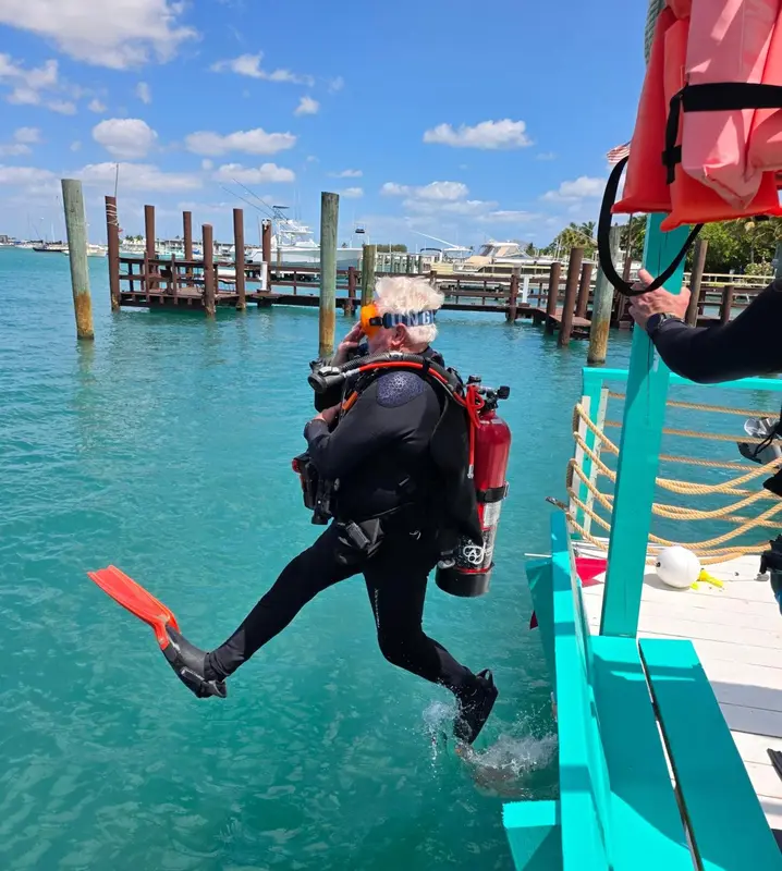 Une personne en combinaison de plongée saute d'un bateau dans l'eau turquoise.