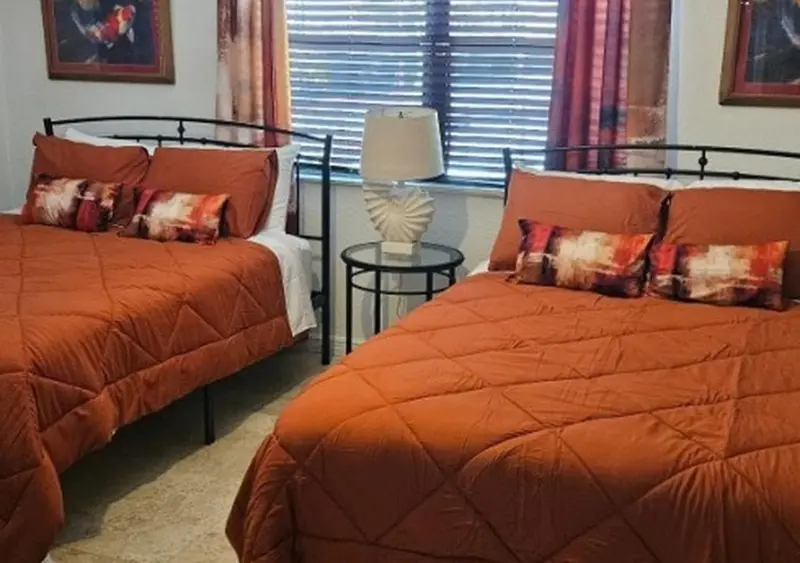 Deux lits simples avec couvertures orange et coussins décoratifs dans une chambre.