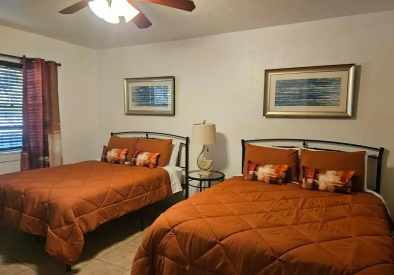 Une chambre avec deux lits simples décorés de coussins orange et de tableaux abstraits.
