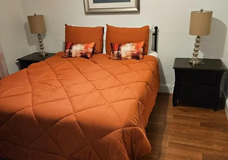 Une chambre avec un grand lit recouvert d'une courtepointe orange et de coussins décoratifs.