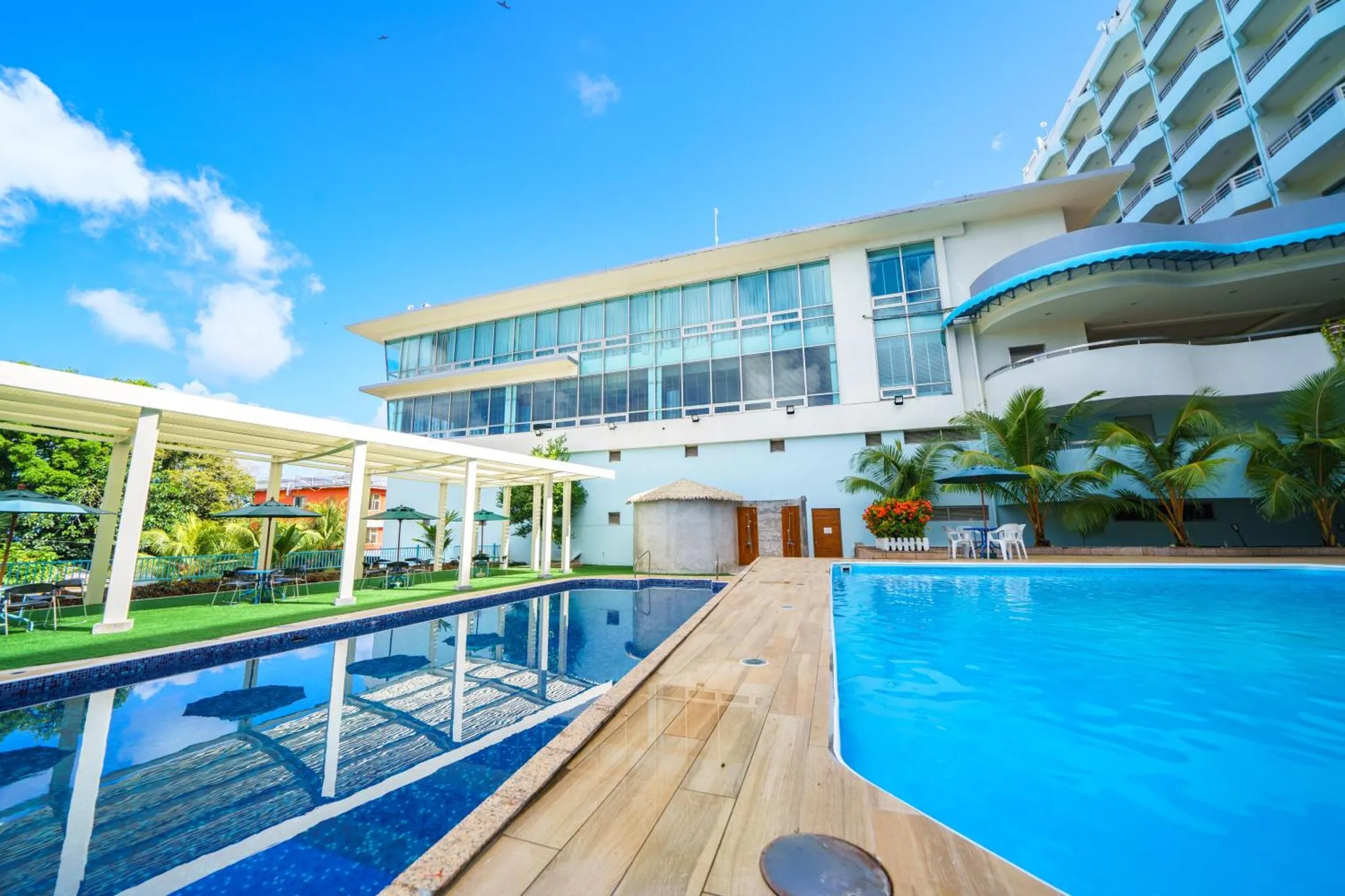Une piscine bleue bordée d'une terrasse en bois, avec un bâtiment moderne en arrière-plan.