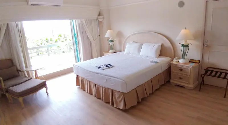 Une chambre lumineuse avec un grand lit et un fauteuil près d'une baie vitrée.