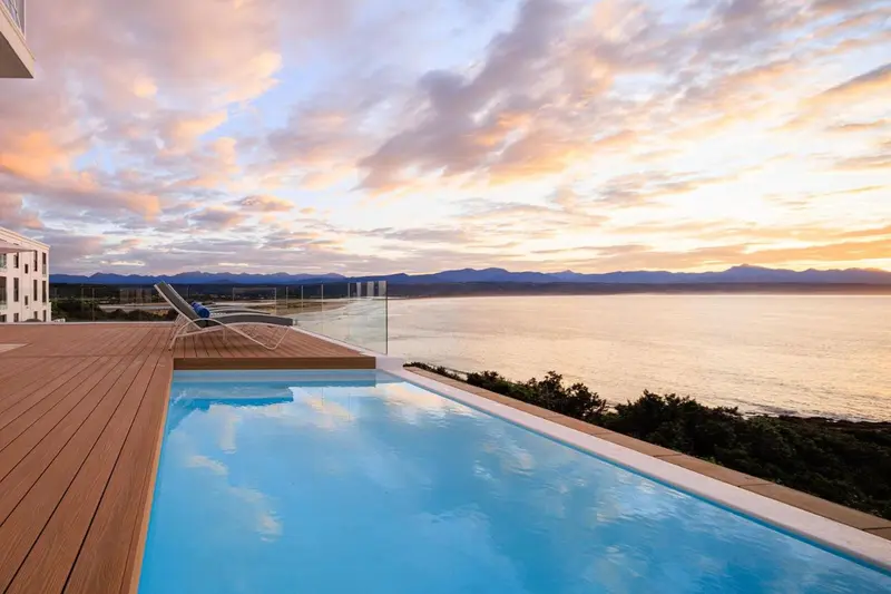 Terrasse avec piscine à débordement donnant sur la mer au coucher du soleil.