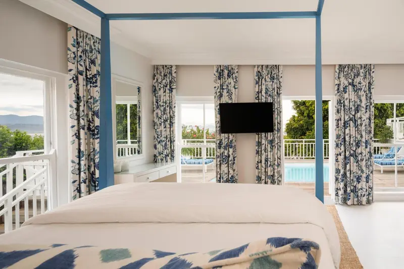 Une chambre lumineuse avec un lit à baldaquin donnant sur une piscine et un paysage verdoyant.