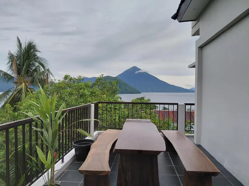 Terrasse avec table en bois et vue sur la mer et les montagnes.